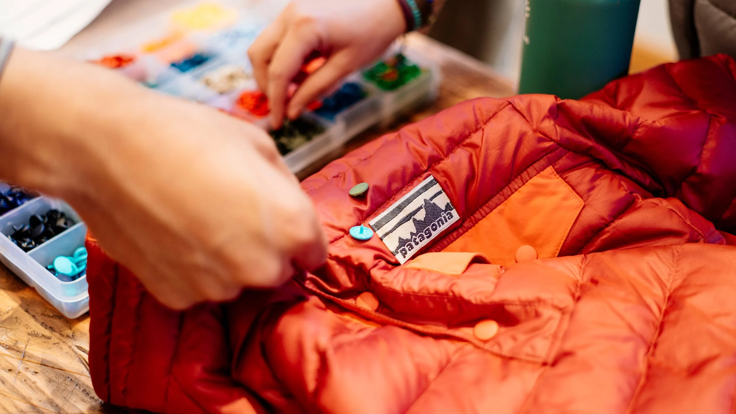 Hands repairing a worn insulated garment beside replacement fasteners.